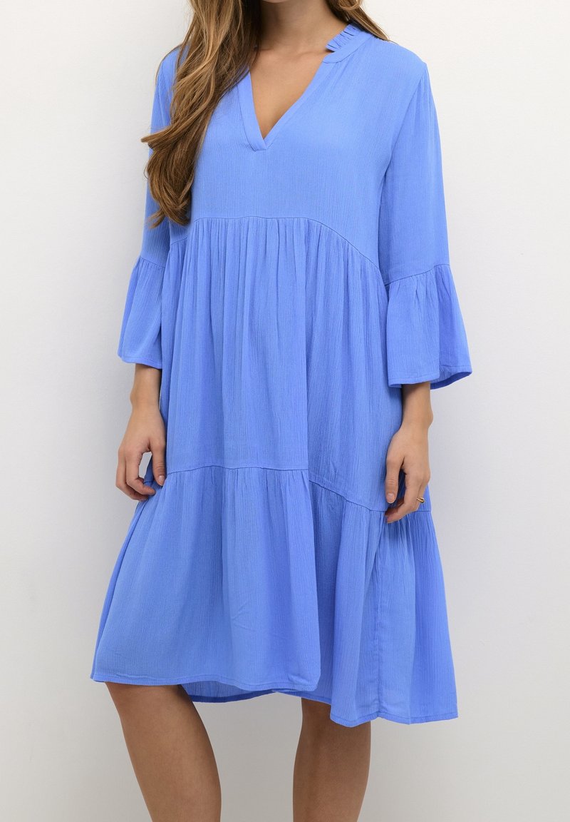Robe bleue, longueur genou, avec un décolleté en V et des manches trois-quarts évasées ; présente une jupe plissée et un tissu texturé.