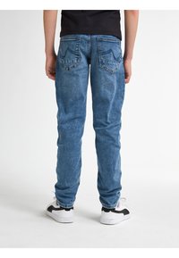 Jeans de denim azul con un corte recto, que presentan dos bolsillos traseros y una textura ligeramente desvaída. Combinados con zapatillas blancas y negras.