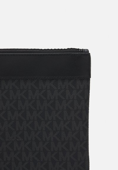 Petite pochette noire zippée avec motif répétitif « MK » et une bande de cuir noir uni en haut.