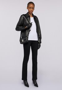 Černá kožená bunda s límečkem, spárovaná s bílým tričkem, černými slim kalhotami, černými rukavicemi a malou černou kabelkou.