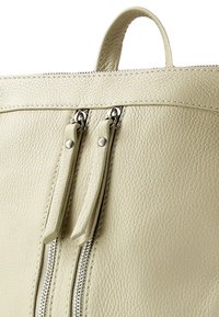 Sac fourre-tout en cuir texturé beige clair avec deux tirettes de fermeture éclair et des finitions en argent. Il dispose d'une poignée supérieure pour un transport facile.