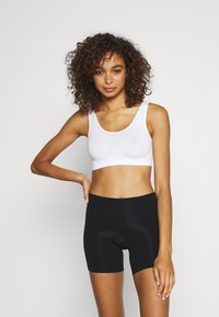 Vit tajt crop top i slät tyg med breda axelband, kombinerad med högmidjade svarta shorts i ettstretchigt material.