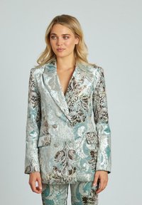 Blazer doppiopetto in tessuto testurizzato con intricatati motivi floreali nei toni dell'acqua e del marrone. Presenta due tasche frontali e un design aderente.