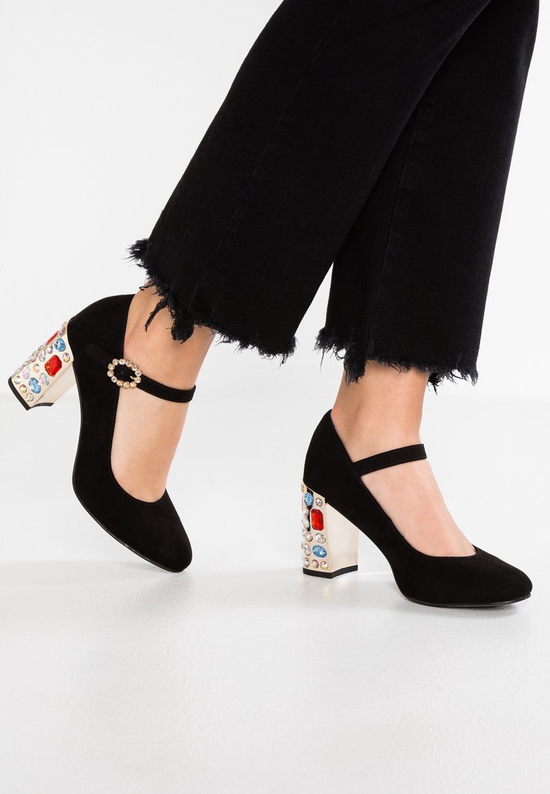 Escarpins Mary Jane noirs avec talons blocs ornés de bijoux et brides à boucle en perles portés avec un pantalon noir raccourci aux bords effilochés.