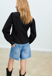 Maglietta nera a maniche lunghe con spalle a sbuffo, abbinata a jeans tagliati blu chiaro e stivali cowboy neri. Stile semplice, minimalismo nei dettagli.
