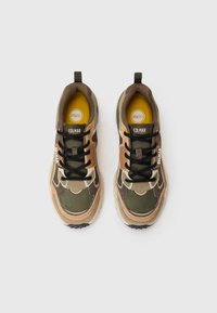 Zapatos de senderismo con un patrón de camuflaje en tonos de marrón y verde, con texturas de malla y ante, cordones negros y plantillas amarillas.