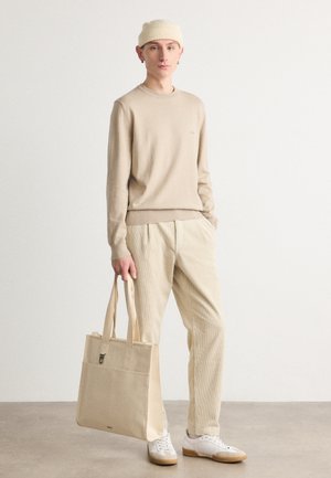 Maglione beige a maglia, pantaloni in velluto a coste e borsa in tela. Texture morbide, tonalità neutre e elementi di design minimalisti.