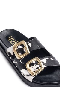 Black and white slide sandal with two wide straps featuring a cow print design. Each strap has a large gold-tone buckle. Textured footbed.