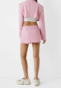 Blazer cropped rosa abbinato a un set di pantaloni corti coordinati. Tessuto morbido con dettagli sartoriali. Maglietta bianca e sneakers chiare completano l'outfit.