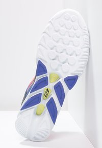 Semelle de chaussure de sport blanche en caoutchouc texturé, avec des accents bleus et jaunes, des motifs géométriques et des trous de drainage pour la traction.