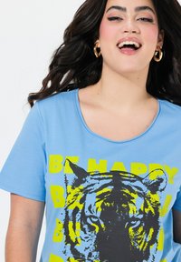 Camiseta de manga corta azul claro con un gráfico de la cara de un tigre en negro y amarillo, con el texto "SE FELIZ" en letras amarillas en negrita.