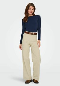 Un haut à manches longues bleu marine associé à un pantalon beige taille haute à jambes larges et une ceinture marron. Présente un design épuré et une texture lisse.