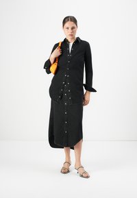 Svart denimskjole med knappestolpe foran, lange ermer og høy-lav søm. Kombinert med en liten oransje veske og grå hælsandaler.