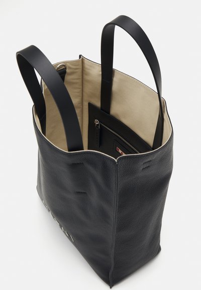 Bolso tote de cuero negro con una superficie texturizada, asas dobles y un forro de tela beige. Cuenta con un bolsillo interior con cremallera para una mejor organización.
