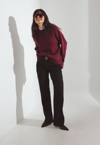 Bordo pulover z rebrastimi manšetami, črne široke hlače z pasom in rjave čevlje s koničastim nosom, s stilom na nevtralni podlagi.