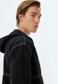 Zwarte hoodie met witte stiksels, voorzien van een trekkoordcapuchon en een relaxed fit. Soepele textuur en minimalistisch ontwerp zonder zichtbare patronen.