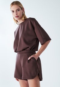 Completo loungewear marrone composto da una maglietta a maniche corte dal taglio rilassato e pantaloni corti abbinati con vita elasticizzata e tasche laterali, realizzato in tessuto morbido.