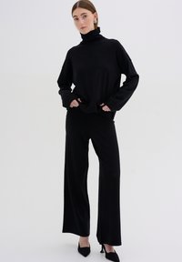 Black turtleneck sweater with long sleeves paired with matching wide-leg trousers, both featuring a smooth, soft fabric texture.