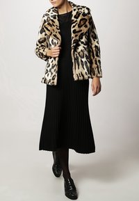 Leopardprint nepsja met een sjawl-achtige kraag; gecombineerd met een zwarte geribde lange rok en zwarte nagelstudschoenen.