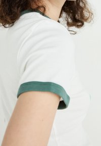 Kortärmad vit t-shirt med grönt ribbat kantband vid kragen och ärmarna, med en slim fit och mjukt bomullsmaterial.