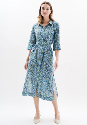 Floral dress in blue, green, and yellow with a collar, three-quarter sleeves, and side slits; features a tied waist. Smooth fabric texture.