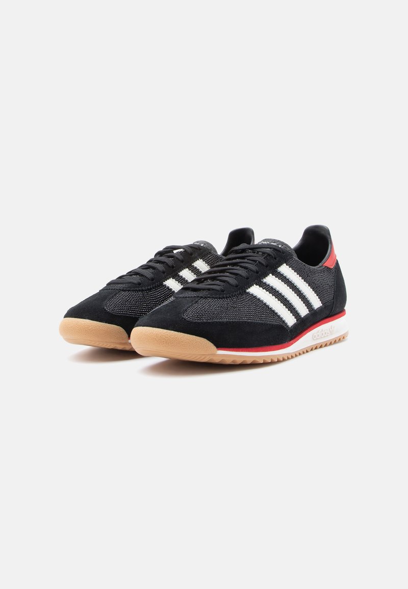 Black athletic sneakers featuring a mesh upper with suede accents, three white stripes, a red heel tab, and a gum rubber sole.