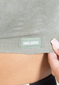 Vihreä, raidoitettu kangas, jossa näkyy avointa merkkiä "SMILODOX" valkoisella. Lähikuva näyttää tekstuurin ja ompeluyksityiskohdat.