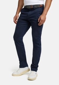 Marineblå chinos laget av mykt stoff, med en smal passform og diskrete sidelommer, kombinert med et mønstret belte og hvite sneakers.