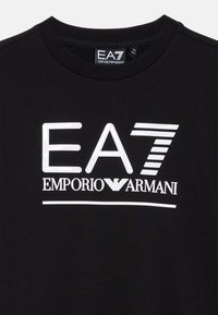 Sudadera de algodón negra con un logo blanco brillante que incluye el texto "EA7" y "EMPORIO ARMANI". Cuello redondo acanalado y mangas cortas.