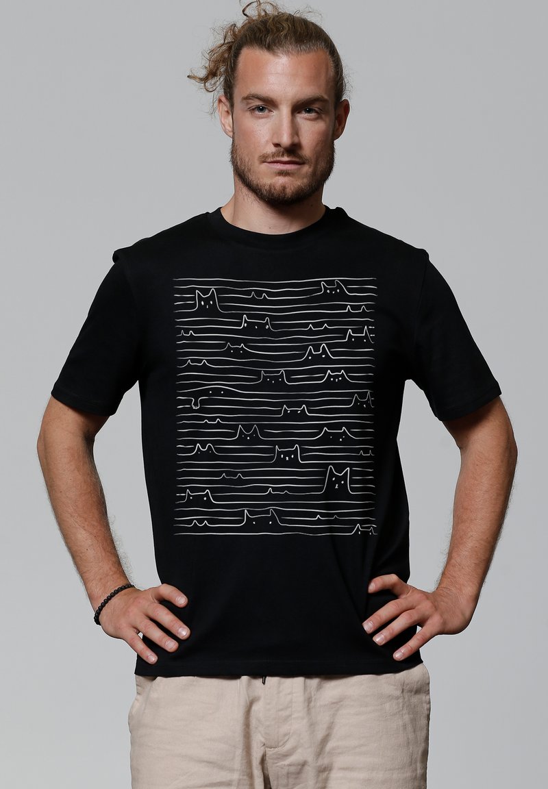 Schwarzes Baumwoll-T-Shirt mit einer weißen Linienzeichnung von Katzen und abstrakten Wellen auf der Vorderseite. Kurze Ärmel und ein Rundhalsausschnitt.