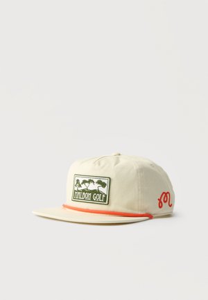 Gorra de béisbol beige con visera plana, parche verde con la inscripción "Malbon Golf", ribete naranja encima de la visera y logotipo bordado en naranja en el lateral.