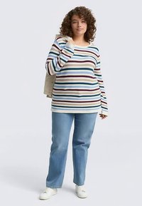 Triibuline pikkade varrukatega särk kreemikas, sinises, lillakas ja burgundia toonis lameda kaelusega; kombineeritud heleroheliste sirgete pükstega ja valgete tossudega.