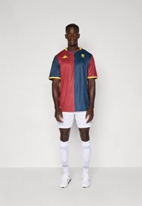 Futbalový dres s červenými a modrými zvislými pruhmi, žltými detailmi a logom leva, v páre s bielymi šortkami a ponožkami v jednofarebnom prevedení.