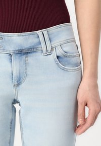 Jean en denim bleu clair avec une texture lisse, doté d'un design classique à cinq poches, d'anses de ceinture et d'une légère décoloration au niveau des hanches.