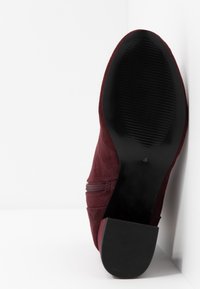 Mörk röd mocka ankelboot med siddragkedja, en texturerad svart gummisula och en låg, fyrkantig klack. Elegant och smidig design.