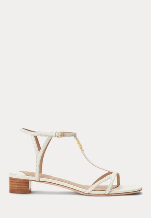 Białe skórzane sandały z regulowanym paskiem na kostkę, w designie T-bar oraz niskim drewnianym obcasem. Posiadają delikatne paski dla wsparcia.