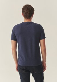 Tumši zils īsroku T-krekls no mīksta, teksturēta auduma ar apaļu izgriezumu un taisnu griezumu, kombinēts ar tumšiem džinsa džinsiem.