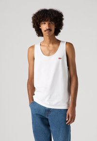 Fehér pamut ujjatlan felső kerek nyakkivágással, kis piros Levi's logóval. Kék farmernadrággal párosítva, laza megjelenésért.
