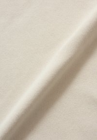 Licht beige breiwerk met een zachte textuur, voorzien van een subtiele ribbelpatroon en een soepele val. Dunne, egale weving zichtbaar.