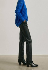 Niebieski dziergany sweter z dużym wzorem o luźnym splocie, zestawiony z czarnymi skórzanymi spodniami i botkami na obcasie z zaostrzonym noskiem. Dopasowany krój.