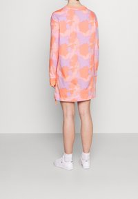 Dlouhé šaty s abstraktním vzorem v pastelově oranžové a fialové barvě; měkká tkanina, uvolněný design, s manžetovými rukávy a bočními šňůrkami.