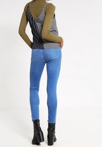 Randig svart och vit linne kombinerat med blå skinny jeans och svarta klackiga ankelstövlar. Fokus på vertikala linjer och kontrasterande färger.