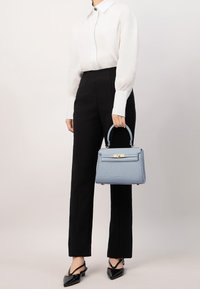 Borsa strutturata di colore blu chiaro con manico superiore e dettagli in oro, abbinata a una blusa bianca e pantaloni neri sartoriali. Scarpe nere con punta.