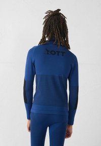 Top sportivo blu con accenti neri, caratterizzato da una texture a coste e logo sul retro. Maniche lunghe e design aderente, adatto per lo sport.