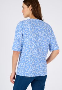 Top corto de manga corta azul con un patrón floral blanco, cuello redondo y dobladillo recto. La tela parece suave con una textura lisa.
