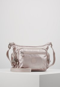 Jasnoróżowa torba na ramię z przednią kieszenią na zamek, regulowanym paskiem, bocznymi przegródkami i małym breloczkiem w kształcie małpki zawieszonym z boku.