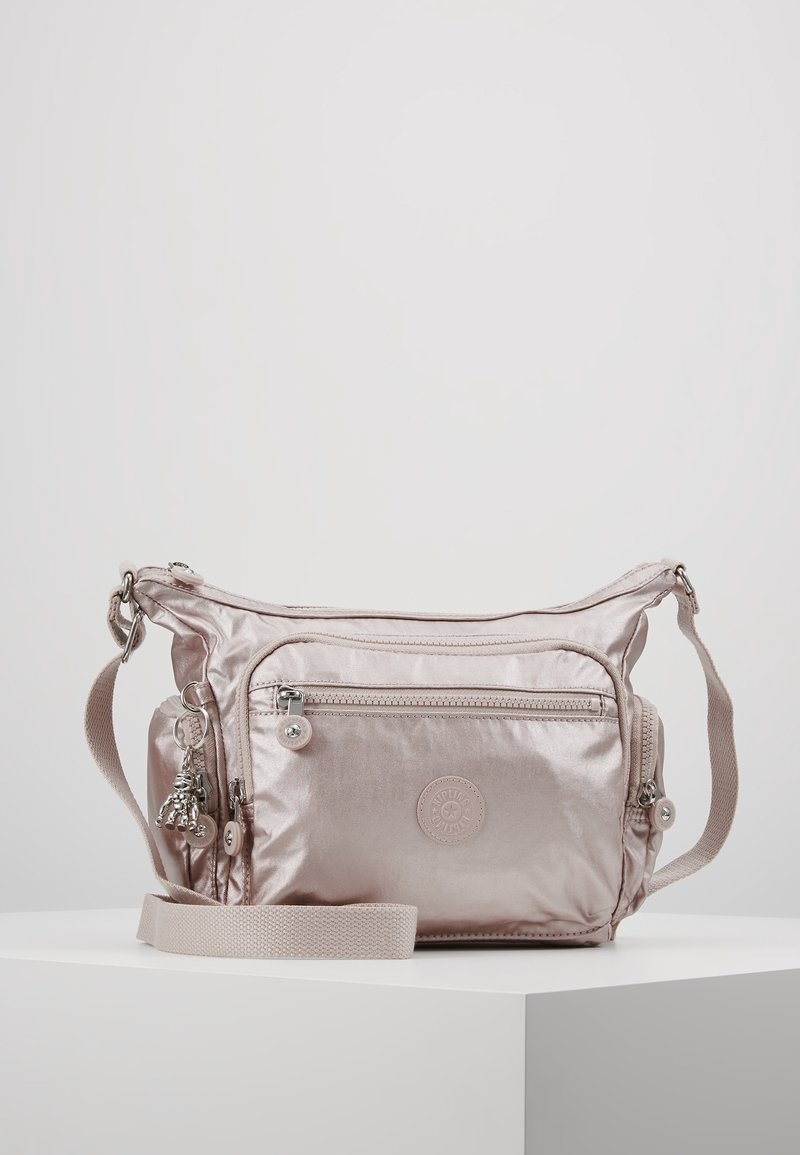 Jasnoróżowa torba na ramię z przednią kieszenią na zamek, regulowanym paskiem, bocznymi przegródkami i małym breloczkiem w kształcie małpki zawieszonym z boku.