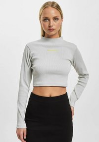 Grå, ribbete langermet crop topp med høy hals, med 'Rocawear'-logo i gult. Kombinert med et svart tettsittende skjørt.