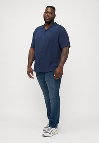 Camisa de botones de manga corta en navy con un corte holgado, combinada con jeans ajustados azules y zapatillas grises. Textura suave, sin patrones.