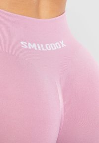 Leggings fucsia a vita alta con texture a costine. Presentano un logo bianco "SMILODOX" sulla cintura. Materiale liscio e elastico.
